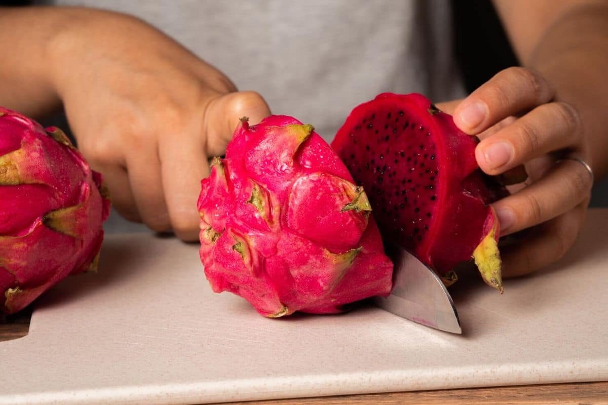 Seseorang memotong buah naga merah di atas talenan