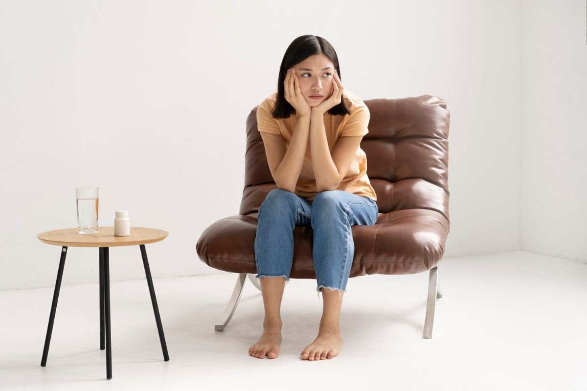 Perempuan duduk di kursi dengan wajah resah