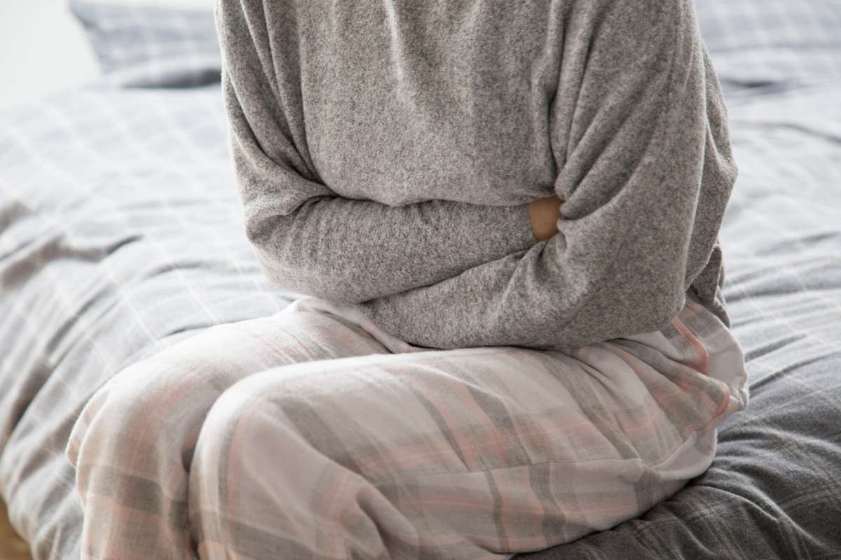 Perempuan duduk di kasur memegang perutnya