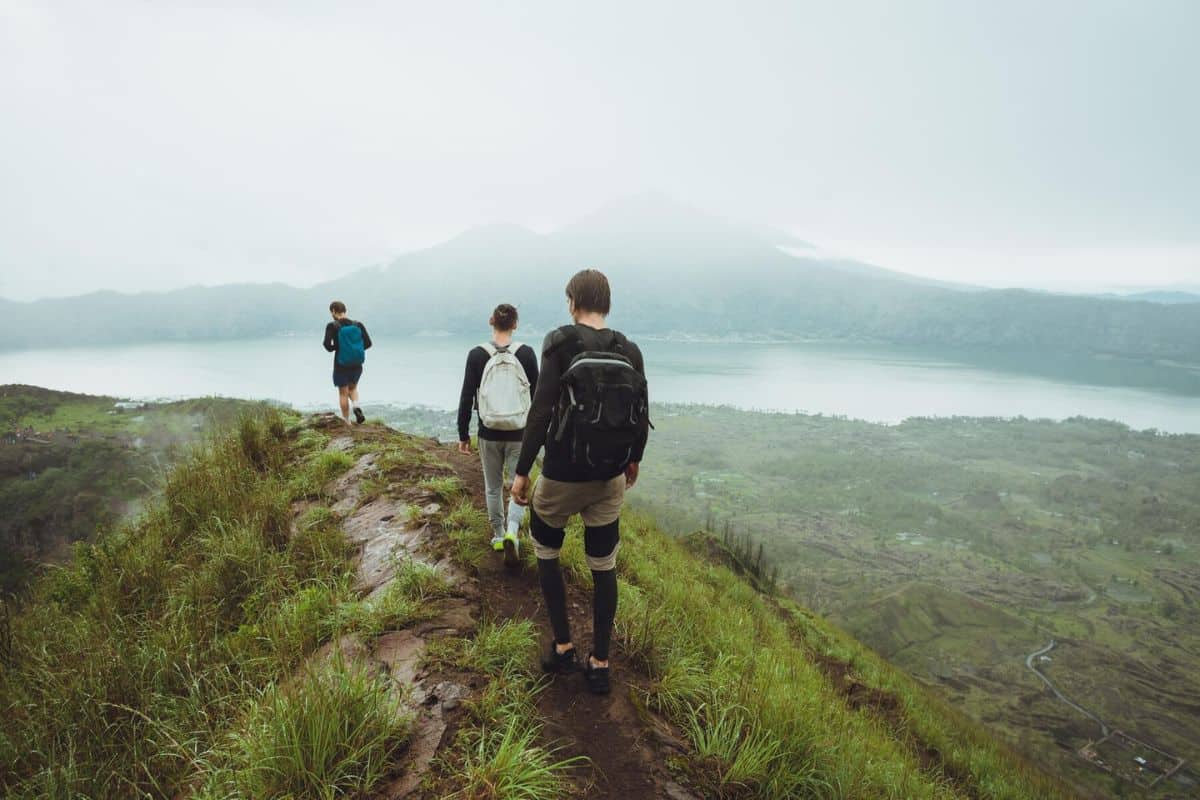 3 Pria sedang hiking dengan latar belakang awan putih dan puncak gunung berapi