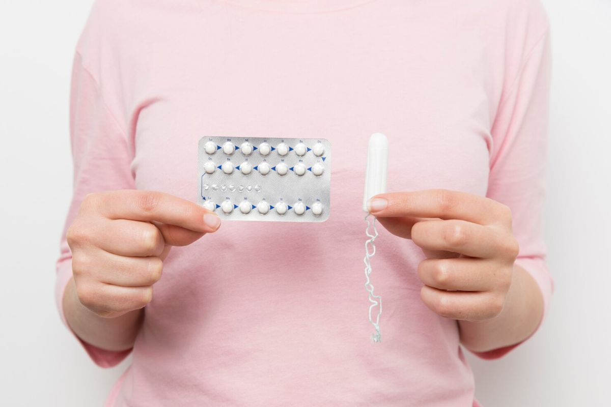 Perempuan memegang pil KB dan tampon