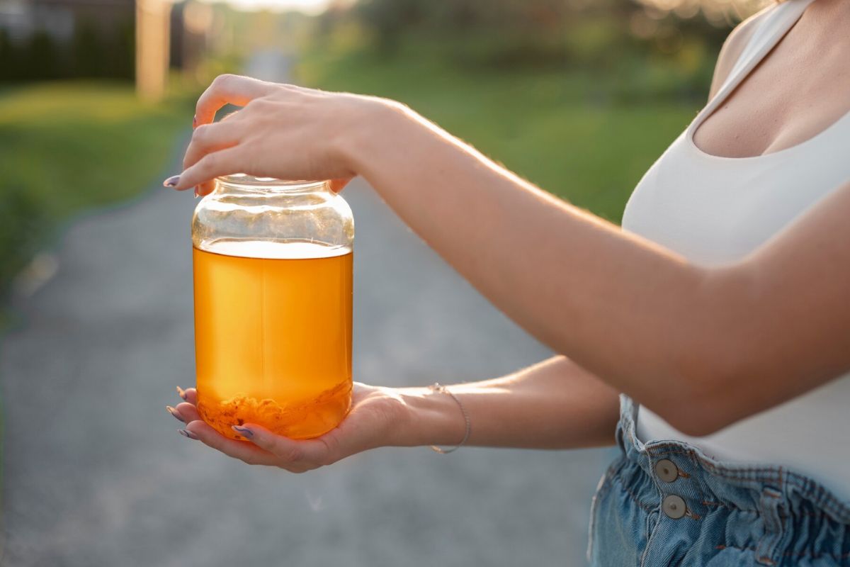 Seorang wanita sedang membawa satu kontainer kombucha di luar ruangan