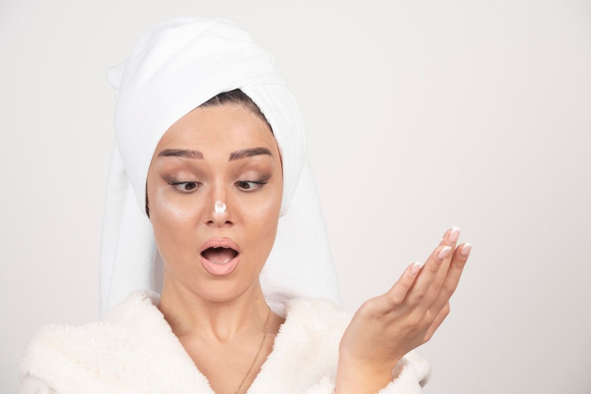 Wanita muda dengan jubah mandi putih mengoleskan krim di hidungnya