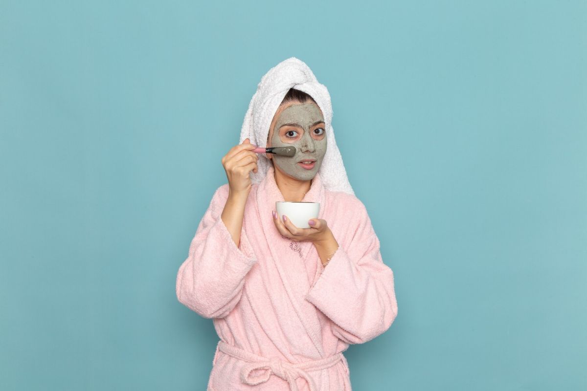 Perempuan dengan jubah mandi mengoleskan masker lumpur