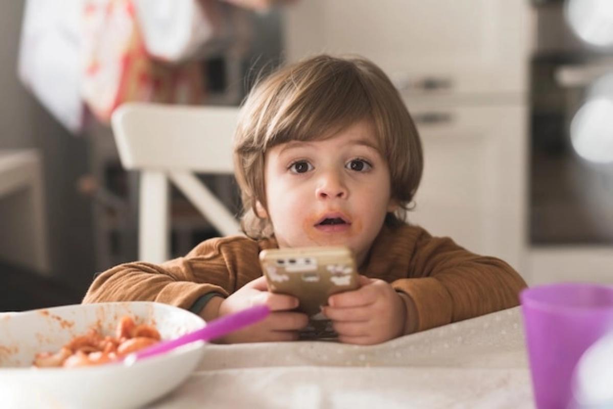 Anak memegang handphone di meja makan