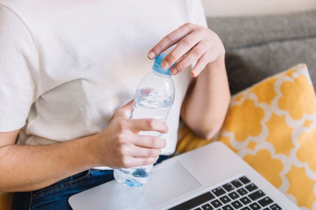 Perempuan di depan laptop sedang membuka botol minum