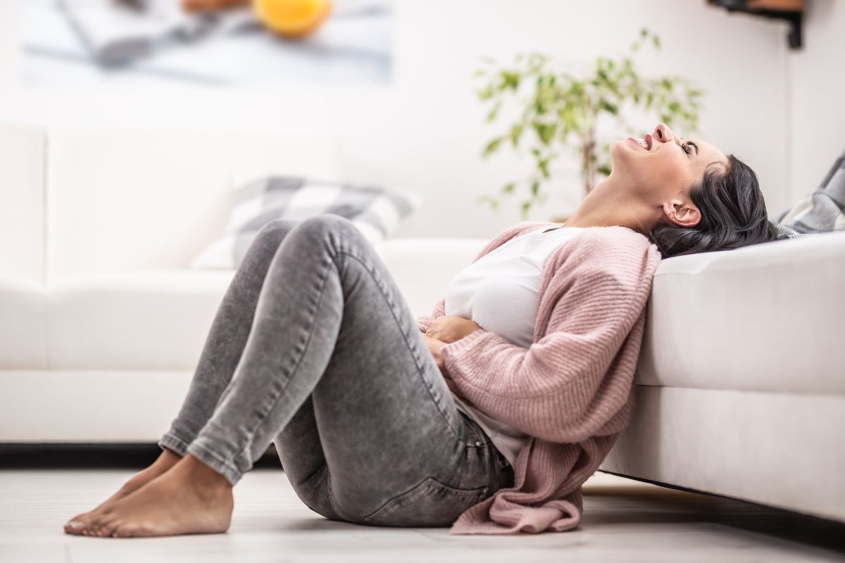 Perempuan memegang perut dan bersandar pada sofa